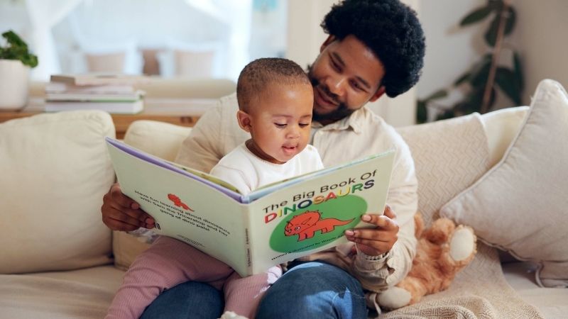 Father and child reading the Big Book of Dinosaurs at home. 