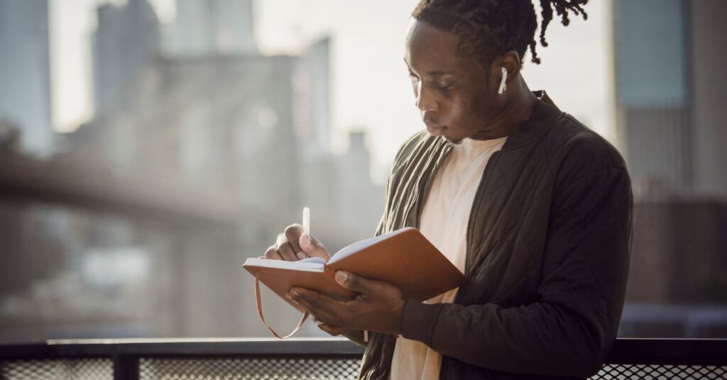 Black male journaling while standing outside 
